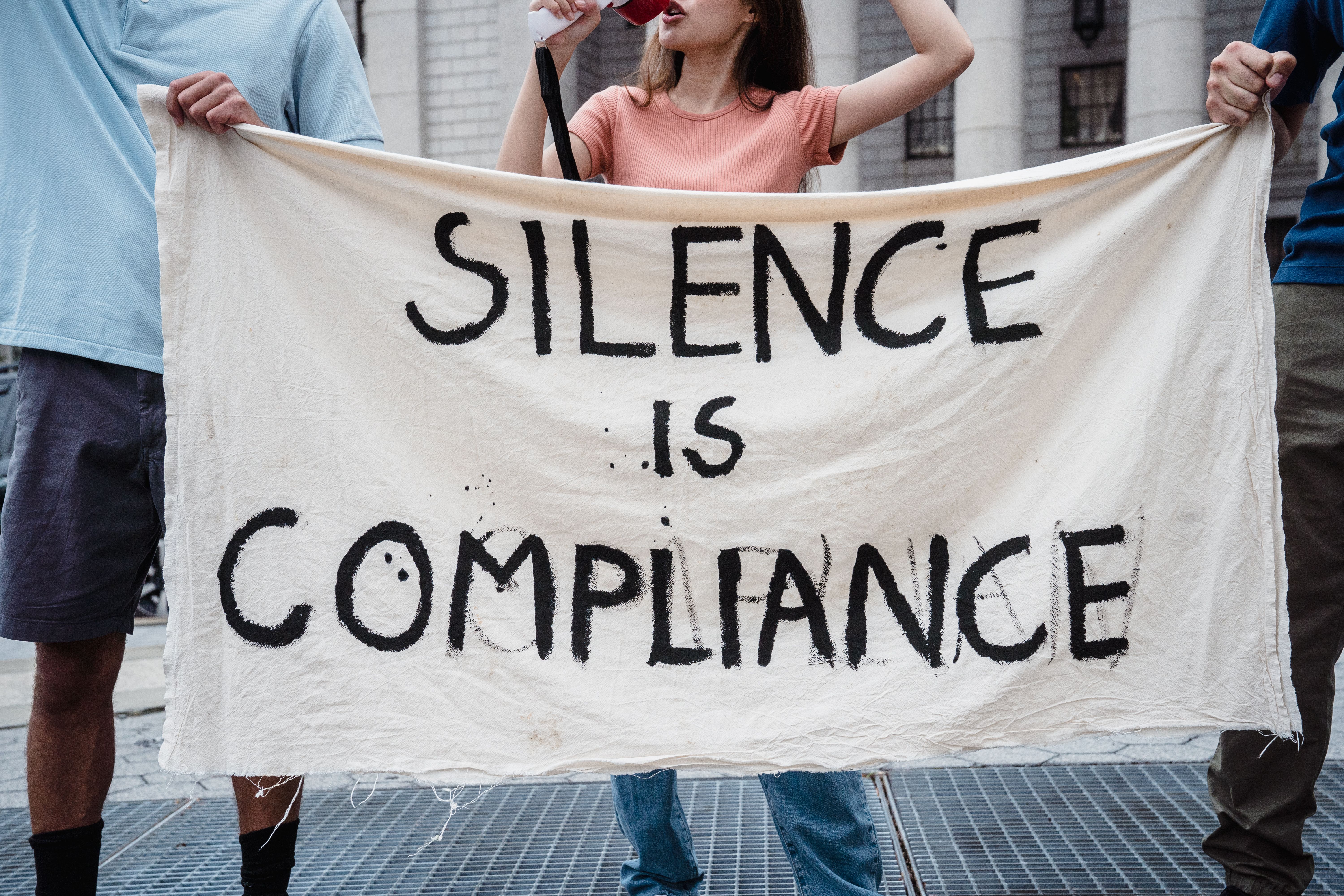 Protesters holding a banner reading Silence is Compliance at a freedom of speech rally