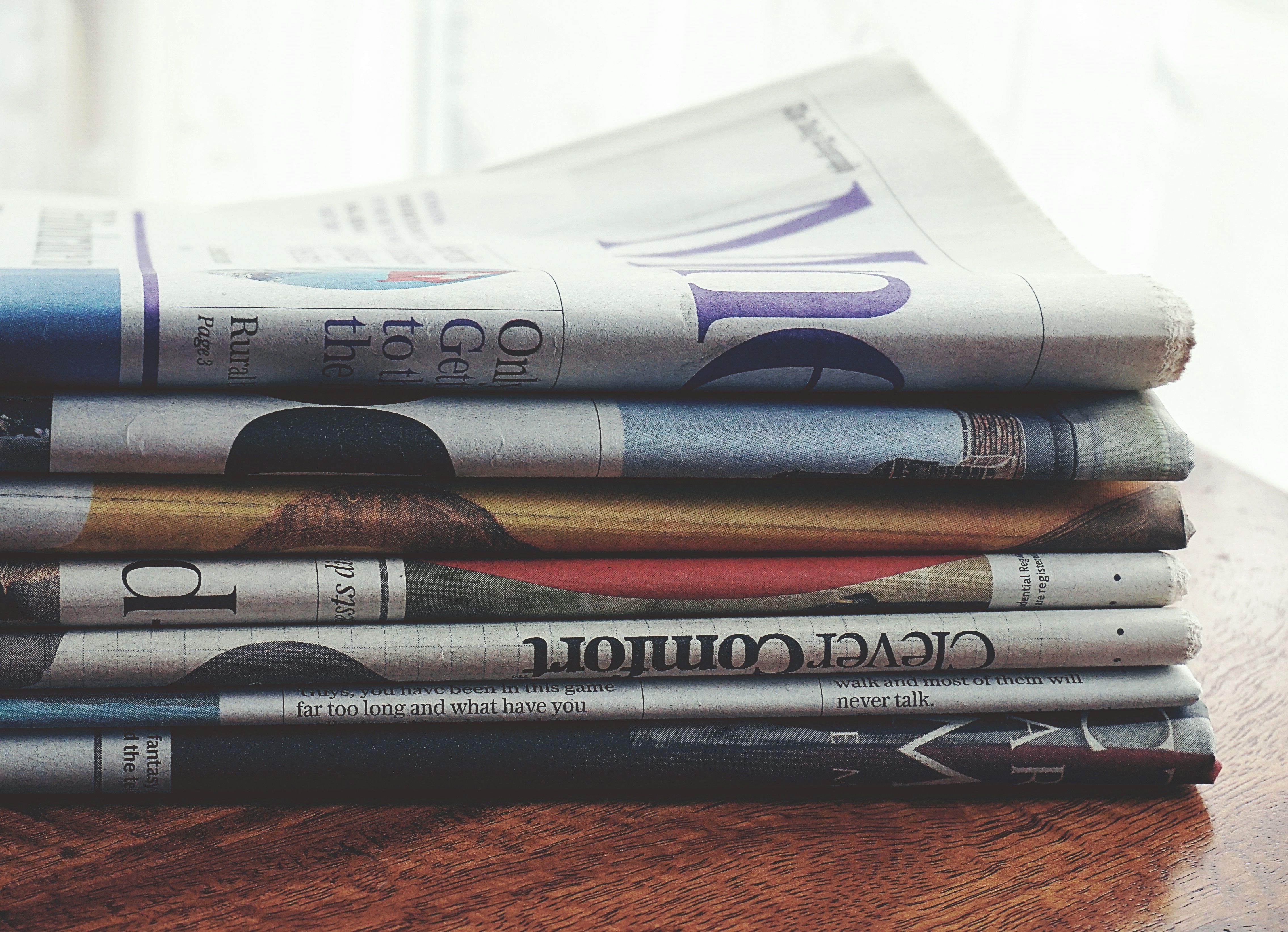 Stack of folded newspapers on a wooden table representing independent journalism