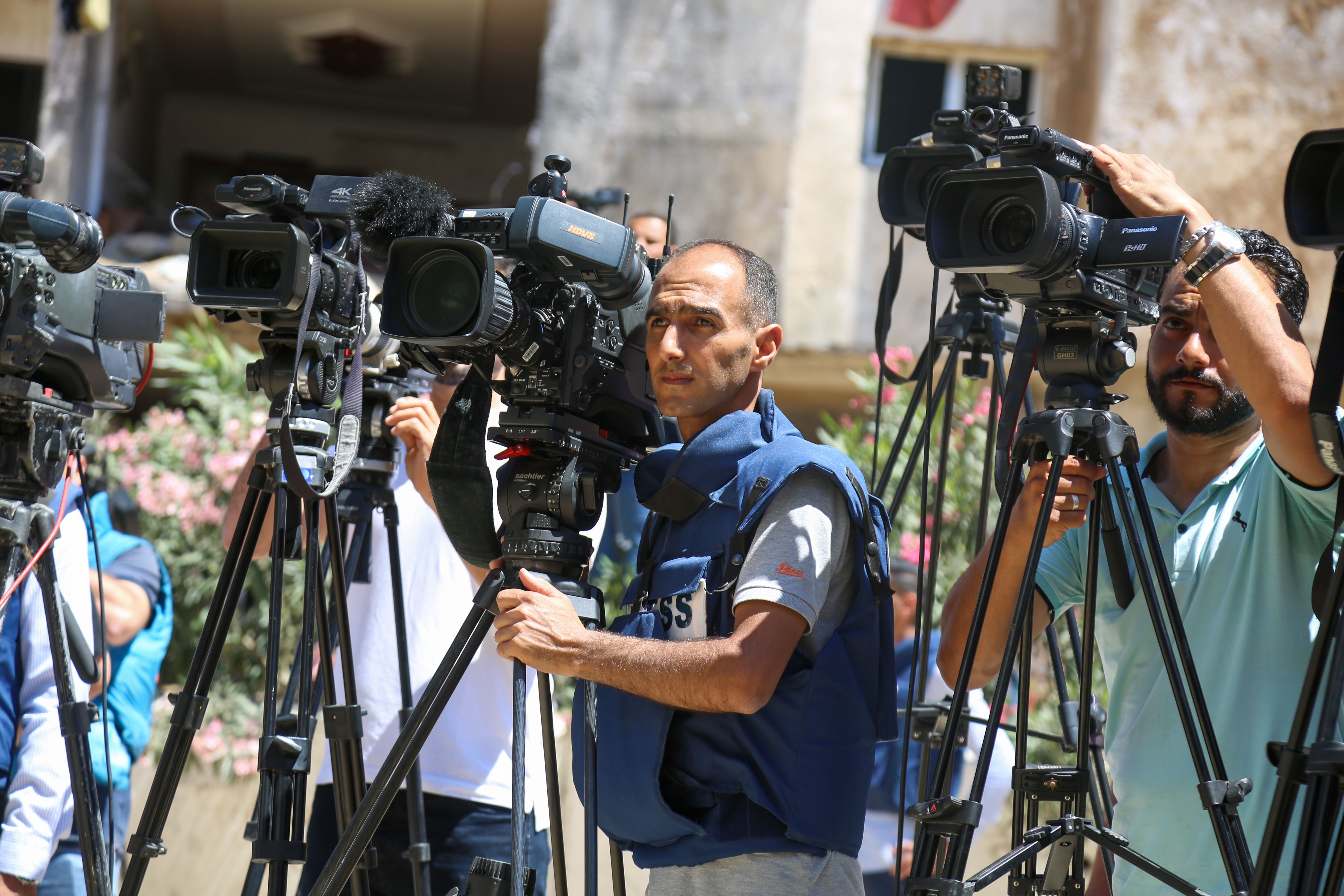 Journalists filming a live broadcast outdoors in a conflict zone, showing risks to reporters