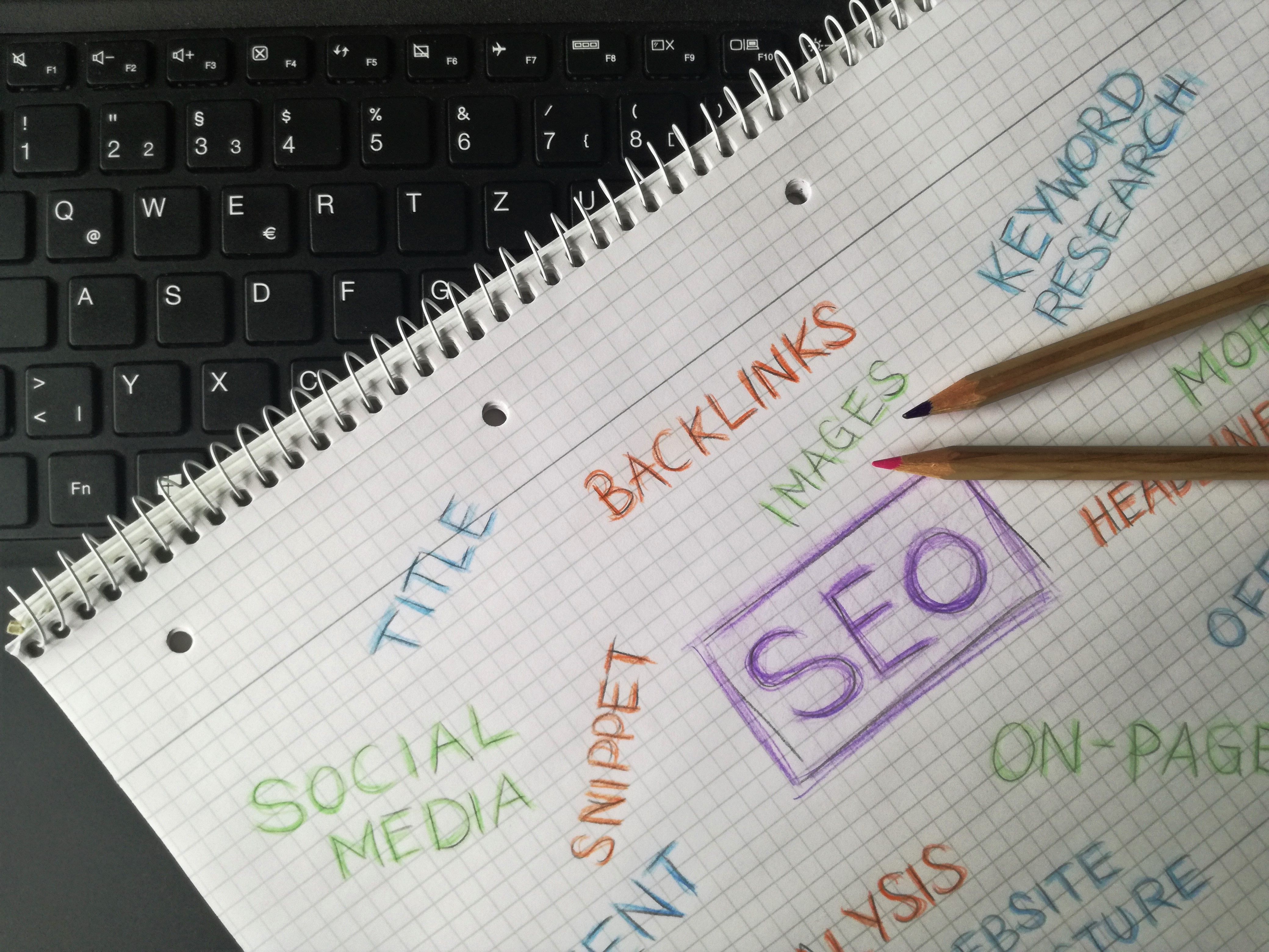 Notebook filled with handwritten SEO terms and keywords beside a keyboard highlighting digital marketing strategy